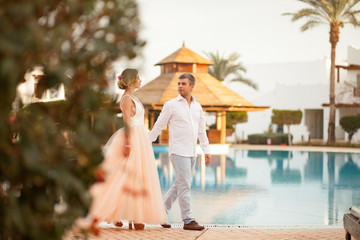 Happy newlyweds walk on the villa next to the swimmimg pool during the honeymoon.