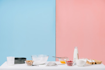 various cooking ingredients and utensils on white kitchen table on bicolor background