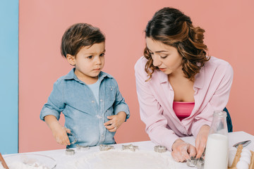 mother with cute little son cooking pastry together at white kitchen table on bicolor background