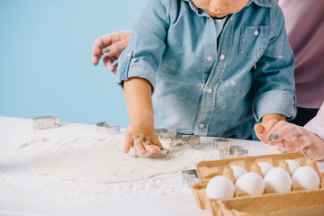cropped view of cute little boy cutting figures in dough together with mother isolated on blue