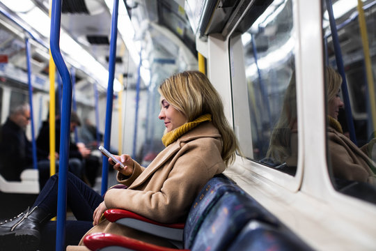Beautiful blonde young woman sitting at metro and typing on her cell phone.