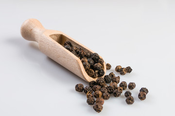 Black pepper peppercorns in wooden scoop isolated on white background. Closeup.