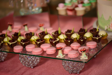 Delicious dessert assortment of playful or themed bite-sized cakes of different shapes, embellished with delicate colorful sugar decorations, displayed on an flat glass or crystal cake stand