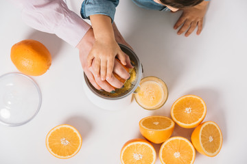cropped view of mother and child squeezing fresh orange juice together on white background