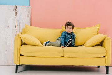 cute little boy in blue jacket and green jeans sitting on yellow sofa