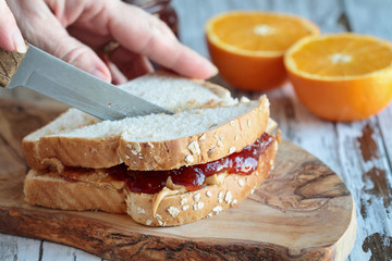 Womans hand cutting a peanut butter and Jelly sandwich on a rustic wooden cutting board. Selective focus on sandwich.