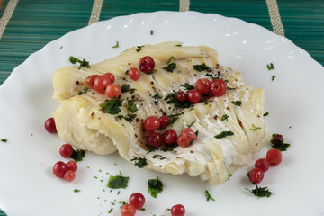 Boiled cod fillet with berries, herbs and spices on a plate close-up. Dietary healthy food.