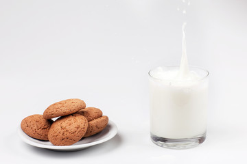 A glass of milk and oatmeal cookies on a light background. Healthy breakfast. Milk spray