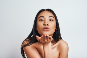 Confident in her beauty. Close up of pretty asian woman blowing a kiss while standing in studio on a grey background