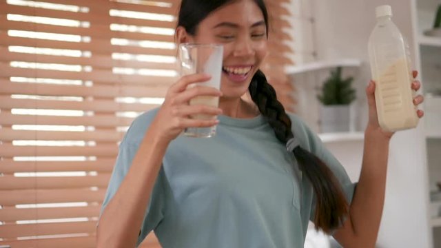 Young asian woman holding glass milk and dancing in kitchen at home.