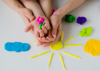 kid play with plastiline. Child's and mother's hands with flower and sun from plastiline. Colorful clay