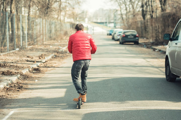 Young fashion guy riding electric scooter on the street, e-scooter kickscooter for personal transportation device in smart city wearing red jacket and working boots
