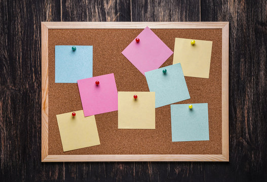 corkboard with pinned multicolored stickers on dark  background