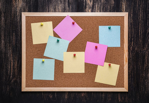 corkboard with pinned multicolored stickers on dark  background