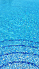 Vertical background shot with copy space of mosaic tiles steps into swimming pool, texture of water surface with ripple effect, concept for summer vacation, spa, relaxation or working from anywhere