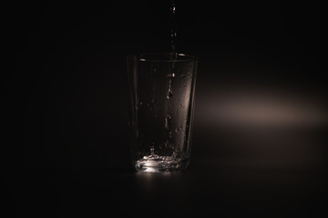 Water is poured into a transparent glass on a dark background