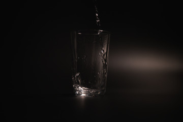 Water is poured into a transparent glass on a dark background