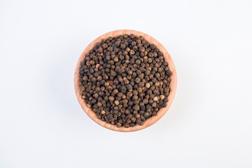 Black pepper peppercorns in wooden bowl isolated on white background. Top view.