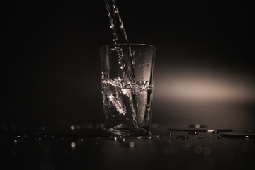 Water is poured into a transparent glass on a dark background