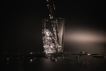 Water is poured into a transparent glass on a dark background