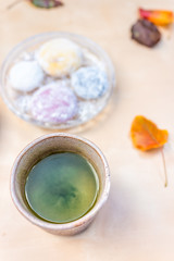 Obraz na płótnie Canvas Green tea cup and mochi rice cake Japanese dessert wagashi colorful daifuku autumn season leaves on table color and vertical flat top view