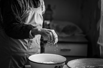  Closeup photo of baker making dough for bread. Hands of an old woman at work with the dough. Retro...