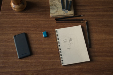 Notebook with drawings and pencil on wooden table.