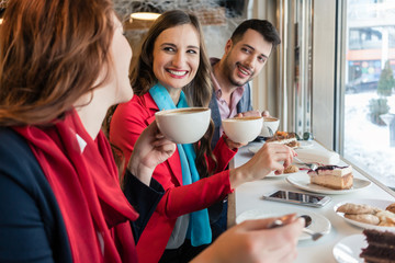 Colleagues smiling while eating delicious cakes during break in a coffee shop