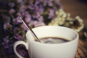 A white ceramic coffee cup with tea spoon on flowers blurred as background, Vintage style