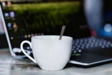 A white ceramic coffee cup with teaspoon on the table and tablet ready for working,Selective focus