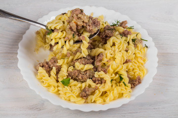 Spirals pasta with minced meat on a white plate on a wooden background.