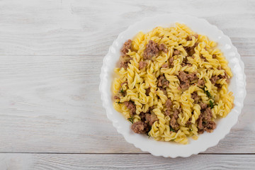 Spirals pasta Bolognese. Tagliatelle with minced meat on a white plate on a wooden background.
