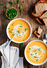 Pumpkin and carrot soup with cream and parsley on wooden background. Top view.