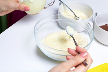 Woman adds condensed milk to coconut chips. Ingredients for dessert are on the table. Cooking sweets with coconut and condensed milk. In a glaze of white and black chocolate.