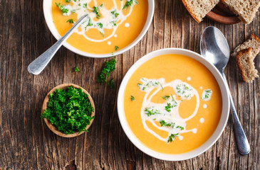 Pumpkin and carrot soup with cream and parsley on wooden background. Top view.