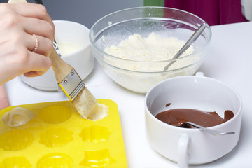A woman lubricates a silicone mold with melted white chocolate. Ingredients for dessert are on the table. Cooking sweets with coconut and condensed milk. In a glaze of white and black chocolate.