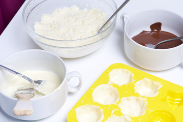 Silicone mold smeared with melted white chocolate. Ingredients for dessert are on the table. Cooking sweets with coconut and condensed milk. In a glaze of white and black chocolate.