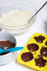 Silicone mold smeared with melted dark chocolate. Ingredients for dessert are on the table. Cooking sweets with coconut and condensed milk. In a glaze of white and black chocolate.