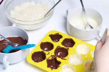 A woman lubricates a silicone mold with melted white chocolate. Ingredients for dessert are on the table. Cooking sweets with coconut and condensed milk. In a glaze of white and black chocolate.