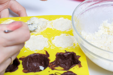A woman puts coconut shavings mixed with condensed milk in a silicone mold, coated with chocolate. Cooking sweets with coconut and condensed milk. In a glaze of white and black chocolate.