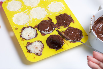 A woman smears chocolate filling coconut and condensed milk. Ingredients for dessert are on the table. Cooking sweets with coconut and condensed milk. In a glaze of white and black chocolate.