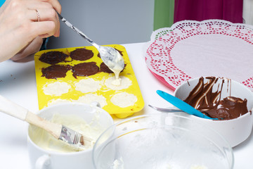 A woman smears chocolate filling coconut and condensed milk. Ingredients for dessert are on the table. Cooking sweets with coconut and condensed milk. In a glaze of white and black chocolate.