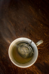 Cup of Tea with infuser in hot smoky water with green tea, mint herbs and honey on a dark wooden background