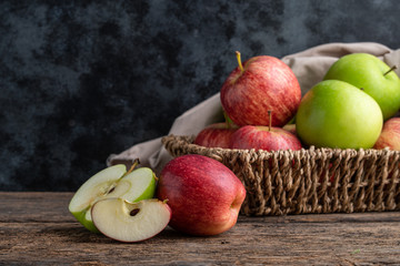 Red and green apples in basket on wooden background.