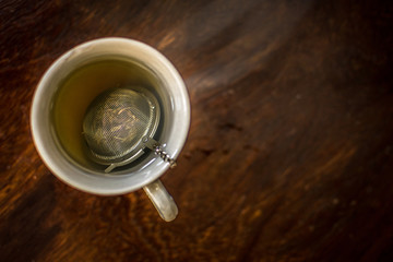 Cup of Tea with infuser in hot smoky water with green tea, mint herbs and honey on a dark wooden background