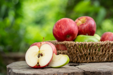 Red and green apples in basket on wooden table with bokeh background.