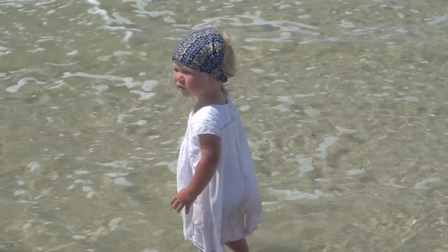 A child is standing in the sea water. Little girl in a white dress walks in the sea water.