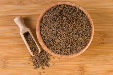 Caraway seeds in wooden scoop and bowl on bamboo desk. Top view.