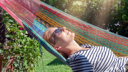 Junge blonde Frau relaxed in einer Hängematte im sonnigen Garten