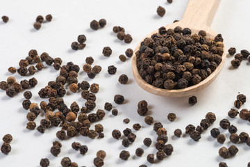 blask pepper peppercorns in wooden spoon isolated on white background. Closeup.